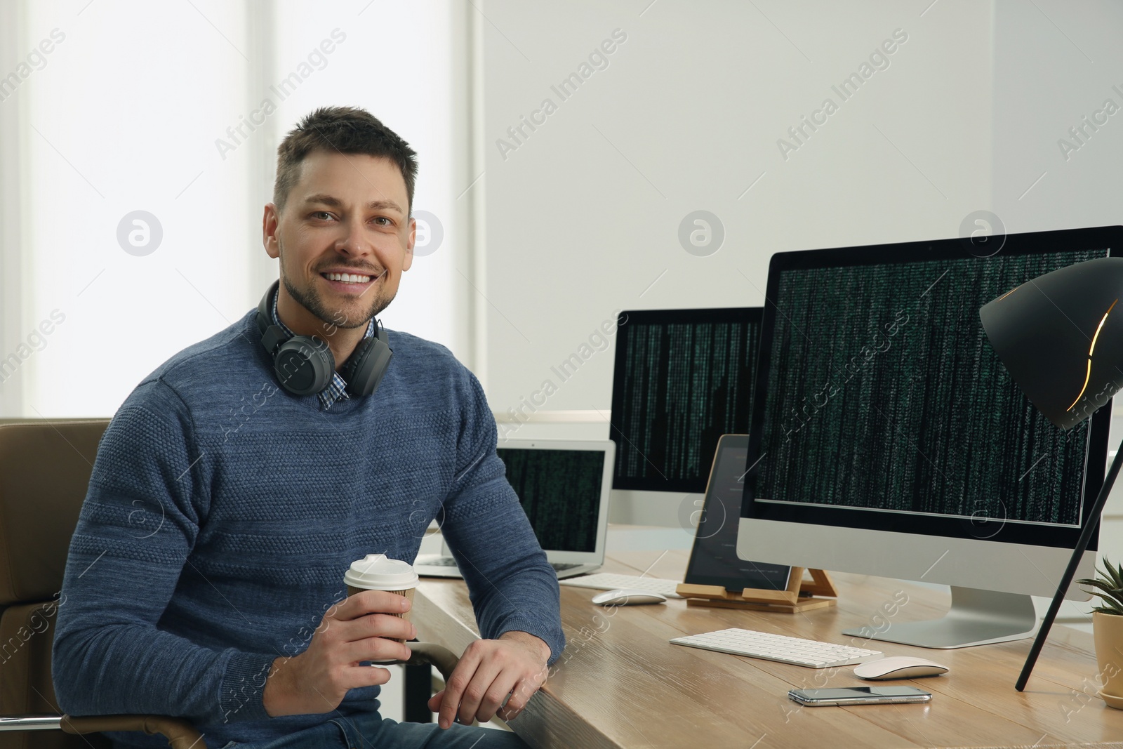 Photo of Happy programmer with headphones and coffee working at desk in office