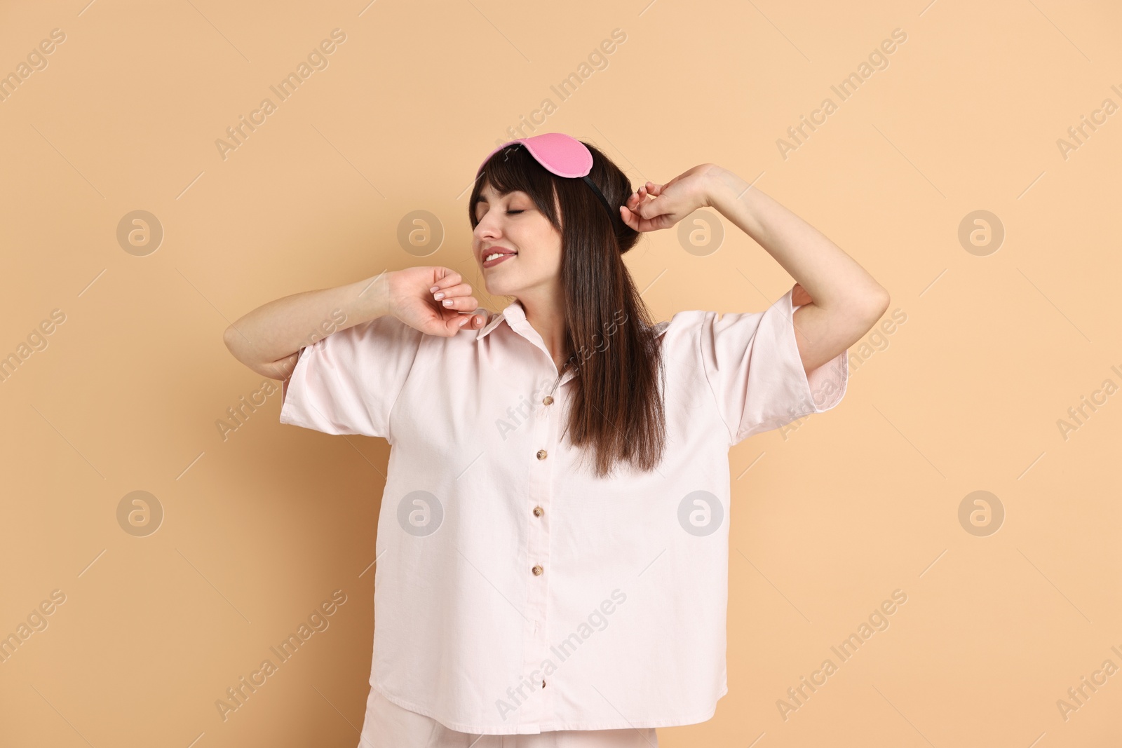 Photo of Woman in pyjama and sleep mask stretching on beige background