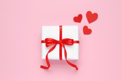 Photo of Beautiful gift box and red decorative hearts on pink background, flat lay