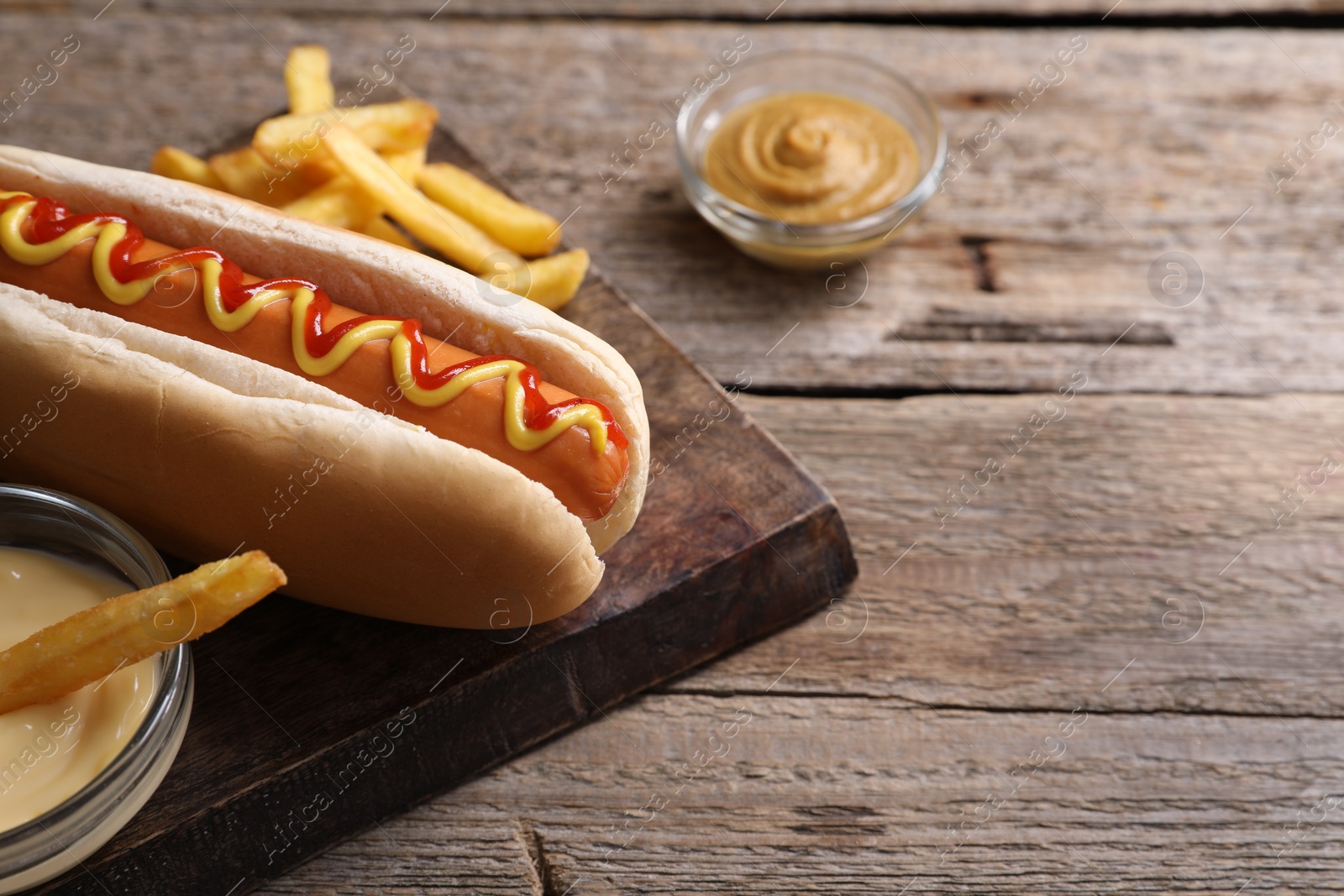 Photo of Delicious hot dog, sauces and French fries on wooden table, closeup. Space for text