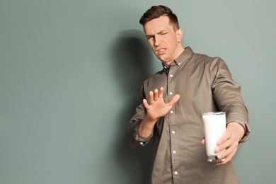 Young man with dairy allergy holding glass of milk on color background