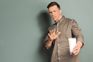 Photo of Young man with dairy allergy holding glass of milk on color background