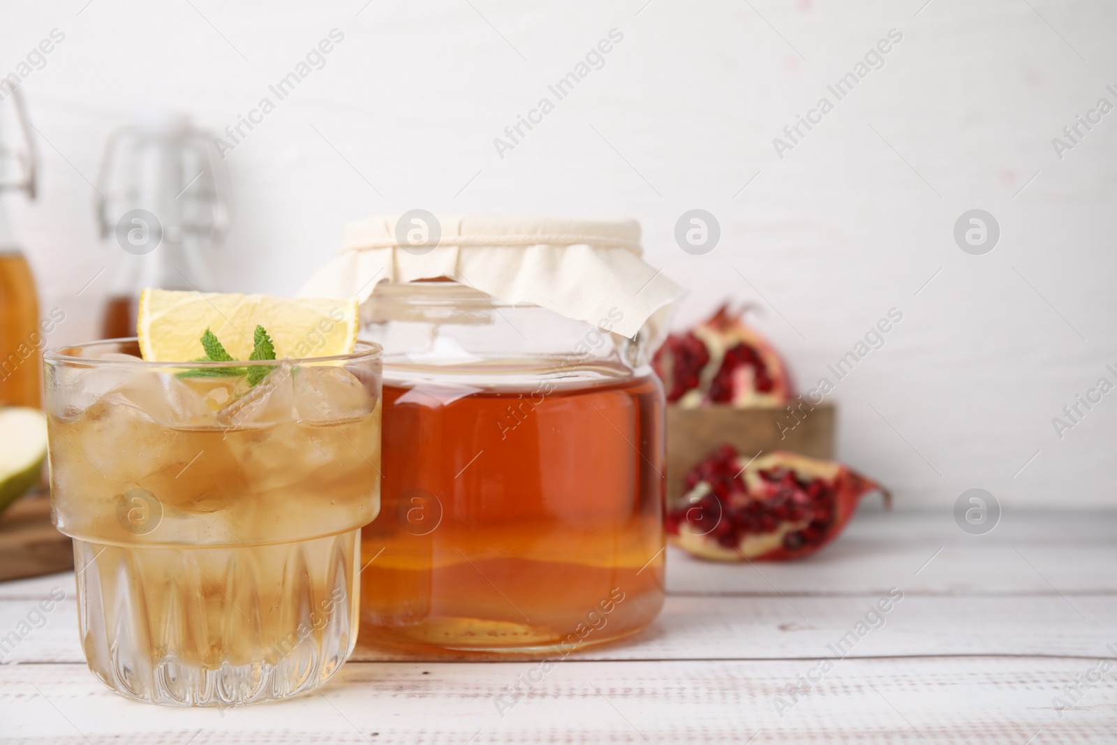 Photo of Tasty kombucha and ice cubes in glass on white wooden table, space for text