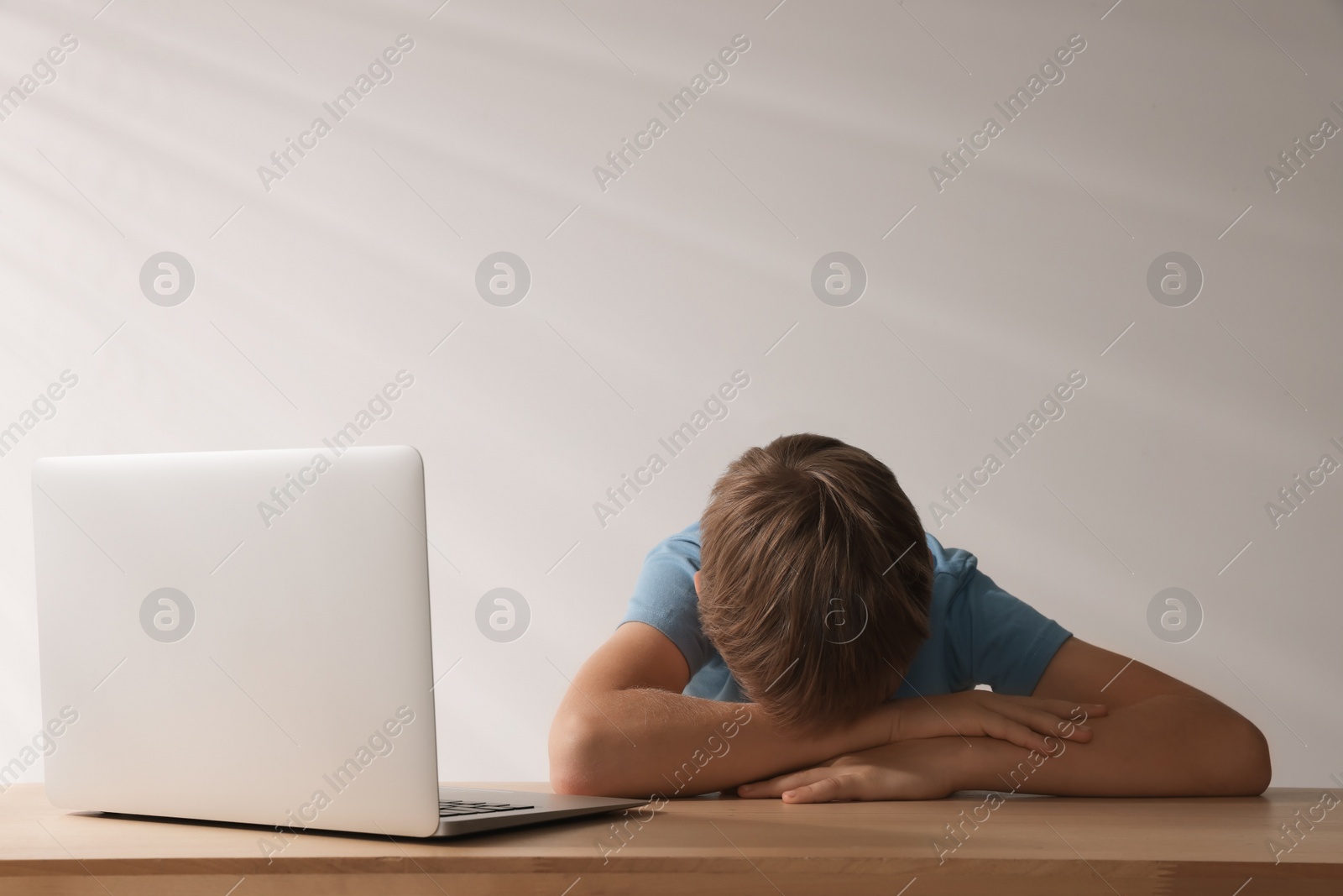 Photo of Upset boy with laptop at table, space for text. Cyber bullying