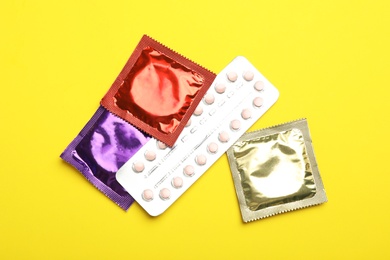 Condoms and birth control pills on yellow background, flat lay. Safe sex concept