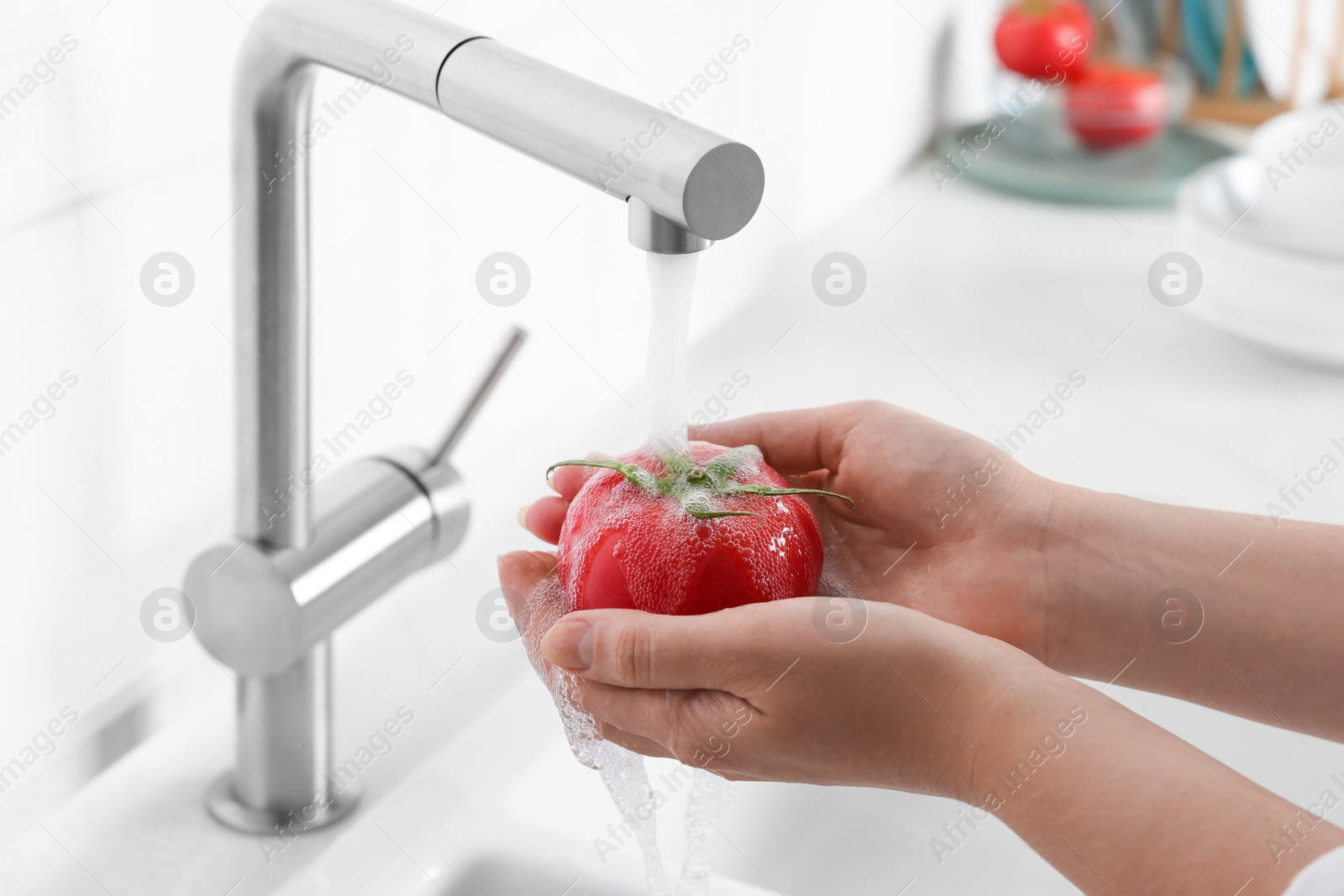 Photo of Woman washing fresh ripe tomato under tap water in kitchen, closeup