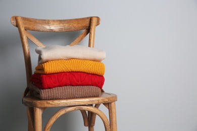 Stack of folded knitted sweaters on wooden chair. Space for text
