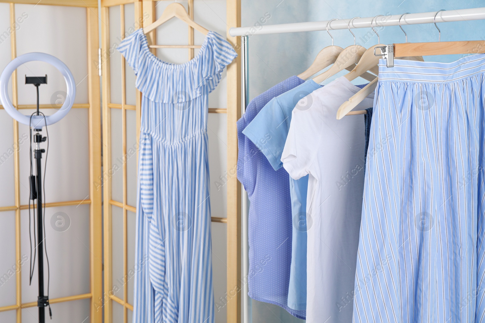 Photo of Rack with different stylish clothes and ring lamp indoors