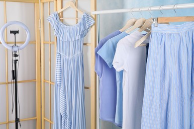 Photo of Rack with different stylish clothes and ring lamp indoors