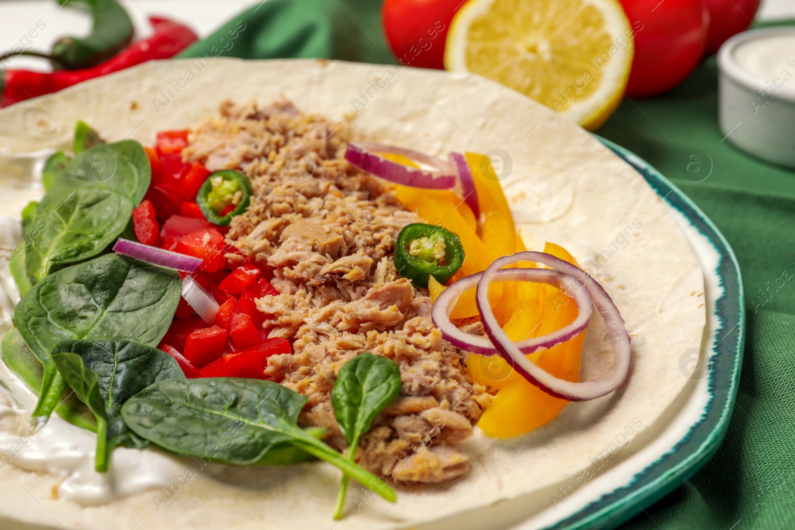 Photo of Delicious tortilla with tuna and vegetables on table, closeup. Cooking shawarma