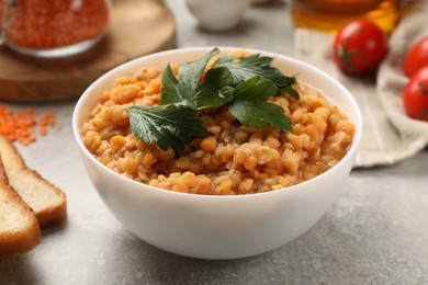 Photo of Delicious red lentils with parsley in bowl on light grey table, closeup