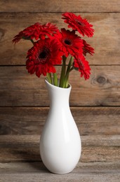 Photo of Bouquet of beautiful red gerbera flowers in ceramic vase on wooden table