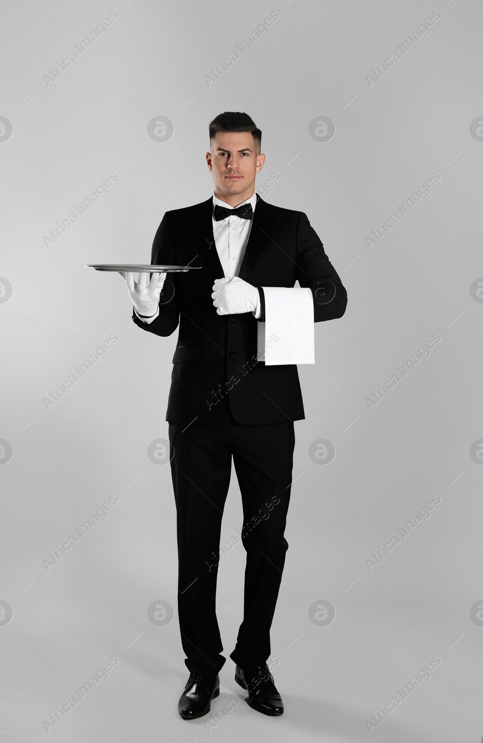 Photo of Handsome butler with tray on light grey background