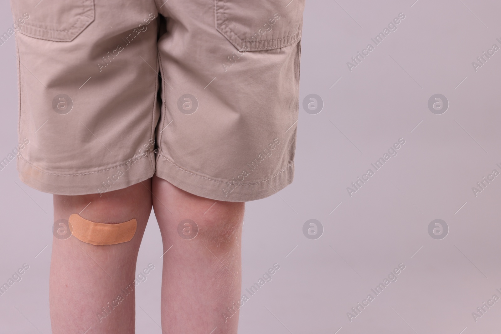 Photo of Little boy with sticking plaster on knee against light grey background, closeup. Space for text