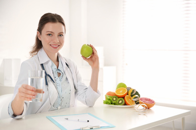 Photo of Nutritionist with glass of water and apple at desk in office. Space for text