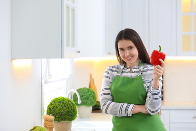 Young woman with apron and bell pepper in kitchen