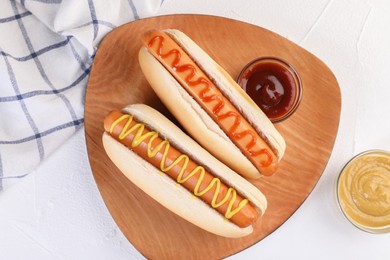 Photo of Tasty hot dogs with ketchup and mustard on white table, flat lay