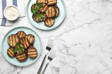 Photo of Delicious grilled eggplant slices and sauce on white marble table, flat lay. Space for text