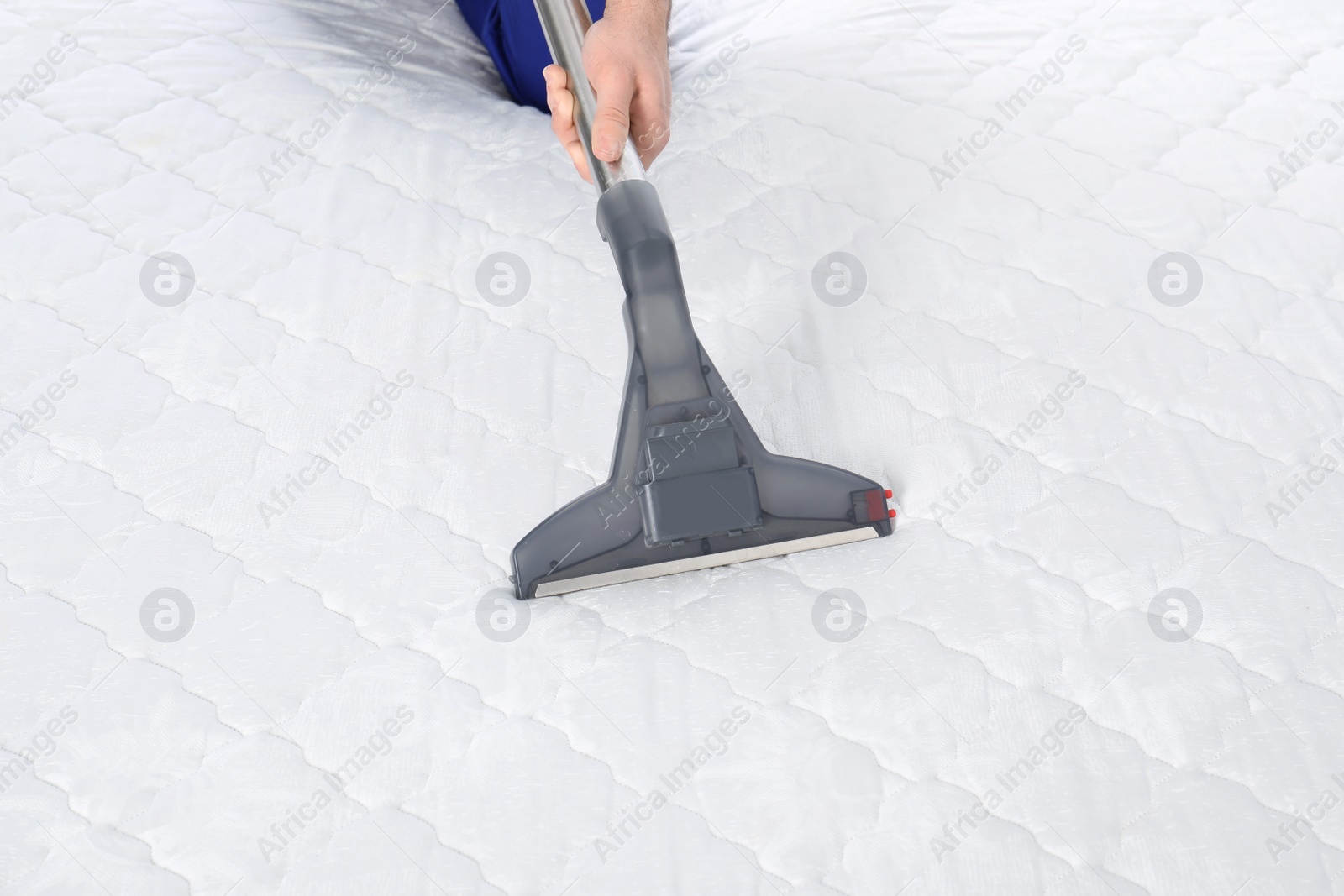 Photo of Man disinfecting mattress with vacuum cleaner, closeup