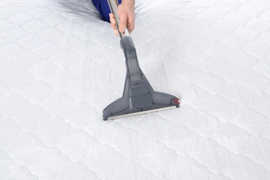 Photo of Man disinfecting mattress with vacuum cleaner, closeup