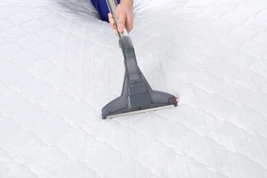 Man disinfecting mattress with vacuum cleaner, closeup