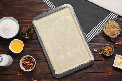 Photo of Making delicious baklava. Baking pan with dough and ingredients on wooden table, flat lay