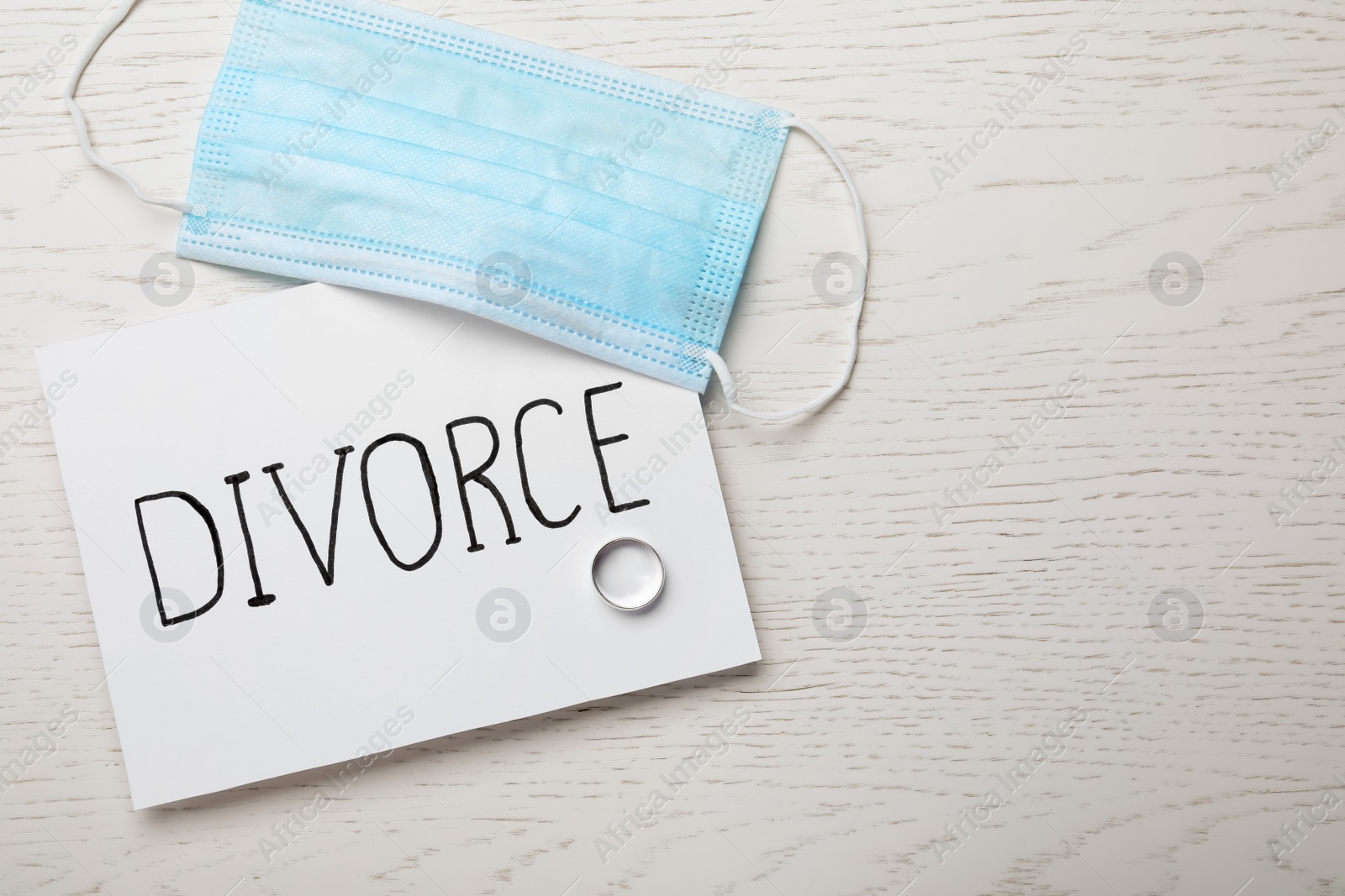 Photo of Flat lay composition with protective mask and wedding ring on white wooden table, space for text. Divorce during coronavirus quarantine