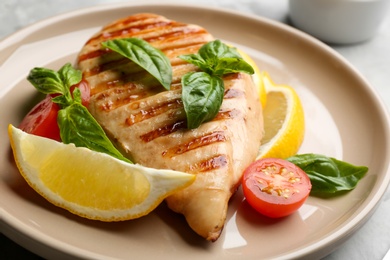 Photo of Tasty grilled chicken fillet with green basil, lemon slices and tomato on plate, closeup
