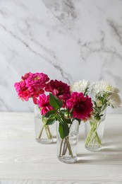Photo of Bouquet of beautiful wild flowers and leaves in vases on white wooden table against marble background