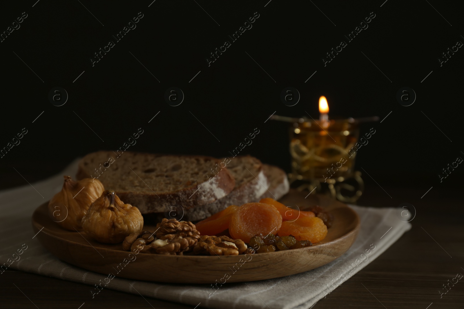 Photo of Bread, dried fruits, walnuts and burning candle on wooden table. Great Lent season