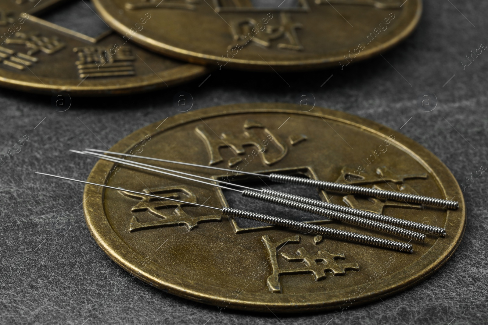 Photo of Acupuncture needles and ancient coins on dark textured table, closeup