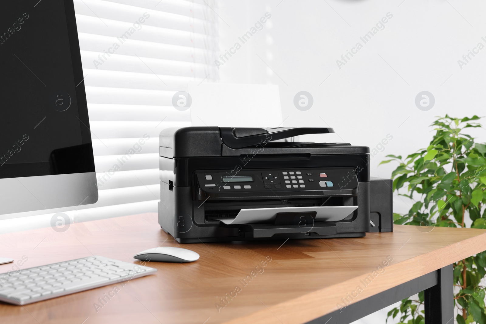 Photo of Modern printer with paper near computer on wooden table in home office