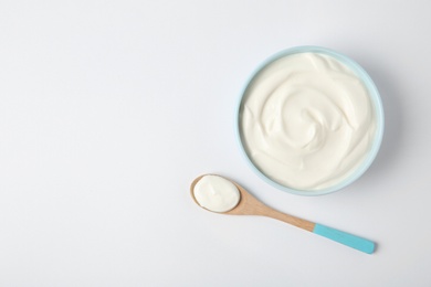 Photo of Bowl of sour cream and wooden spoon on white background, top view