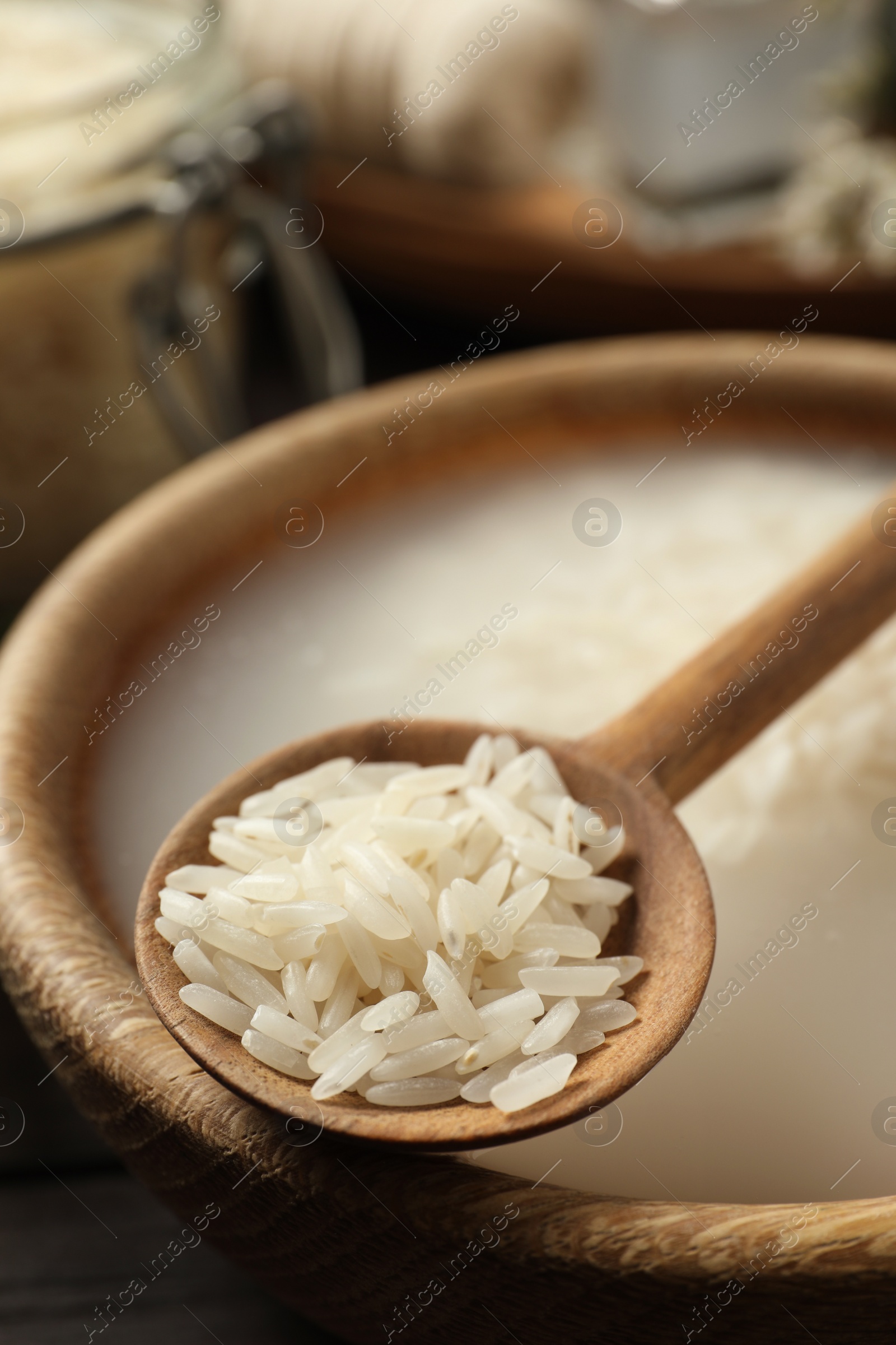 Photo of Wooden bowl with soaked rice and spoon on table, closeup