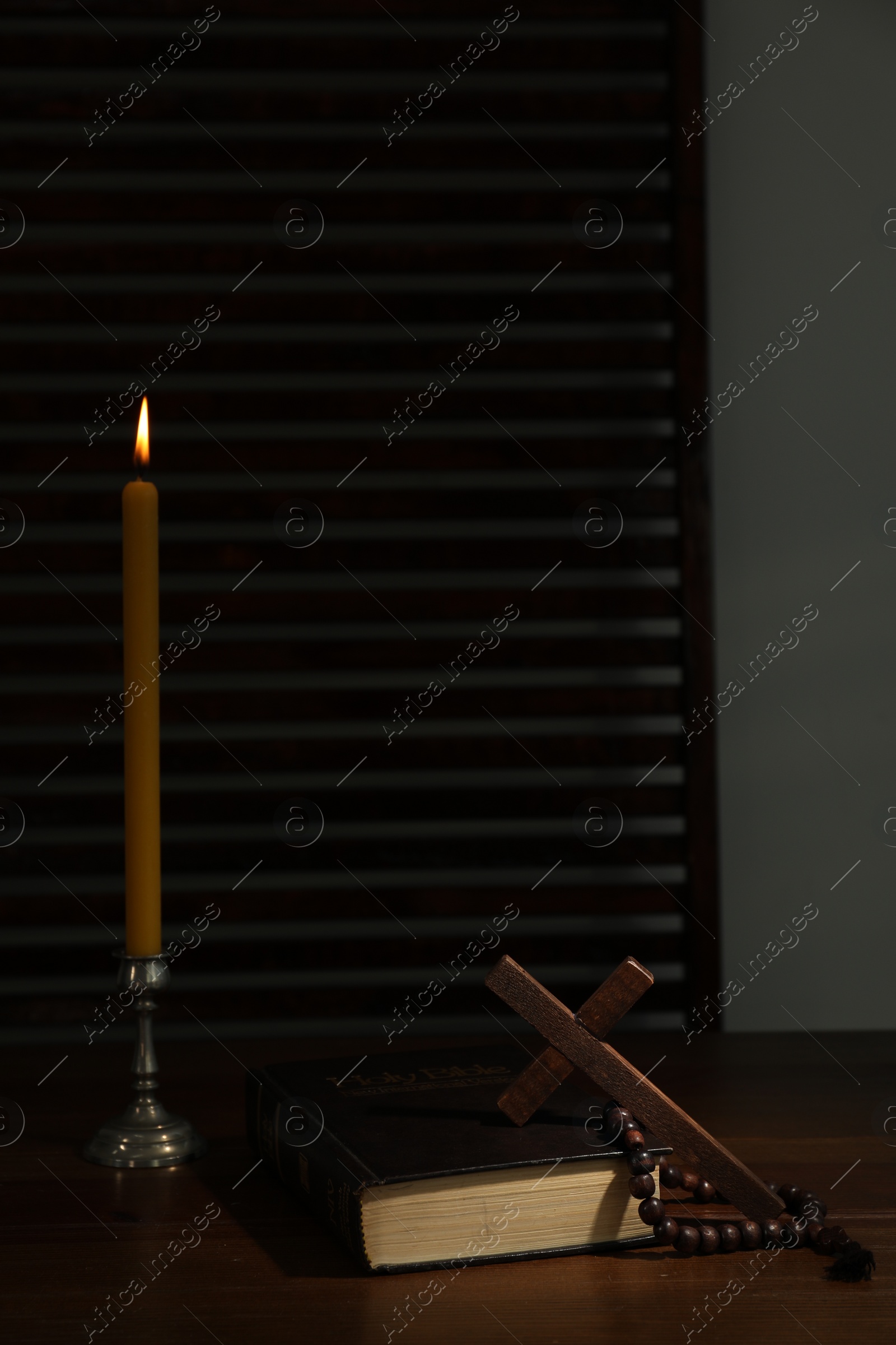 Photo of Church candle, Bible, cross and rosary beads on wooden table, space for text