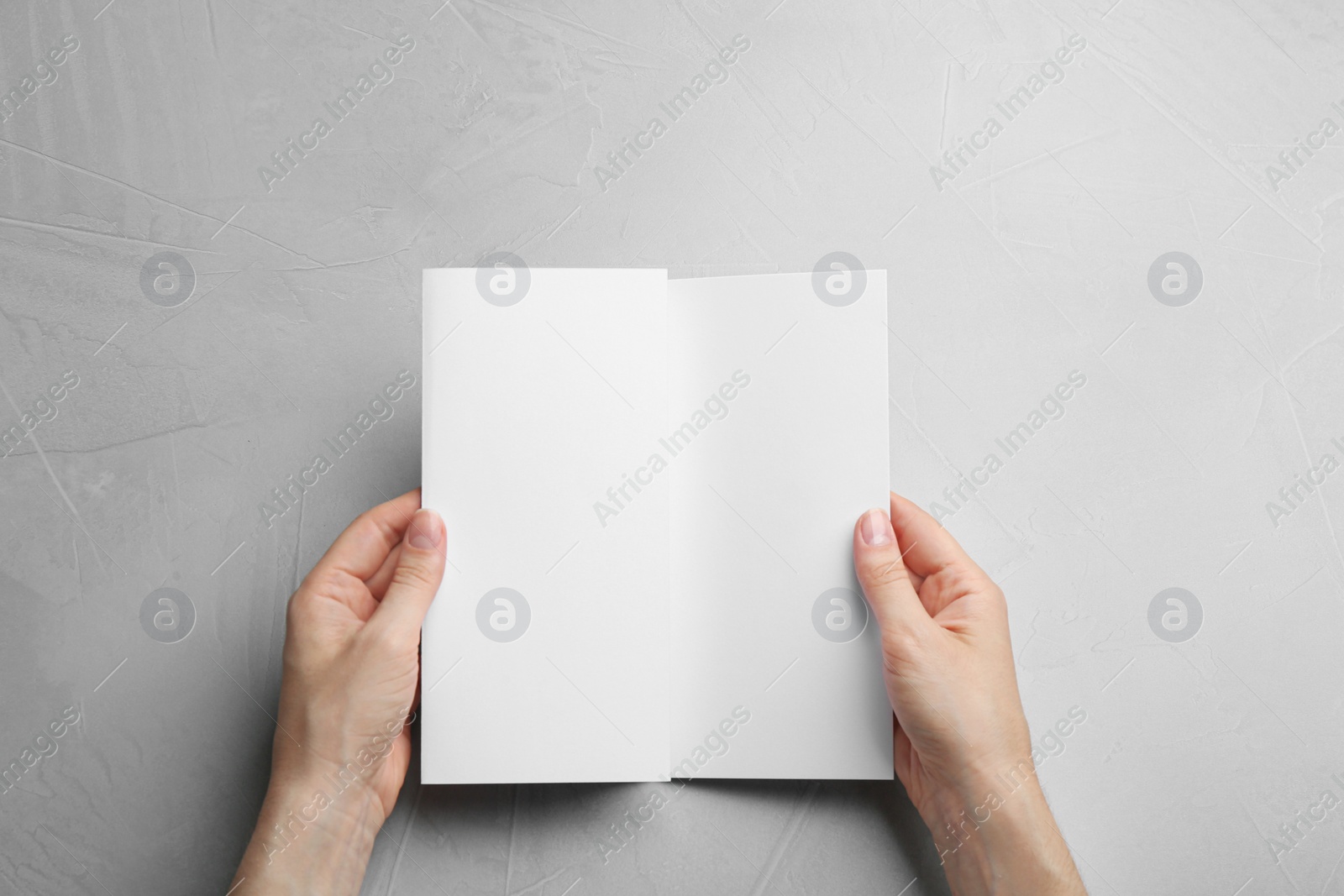 Photo of Young woman holding blank brochure at grey table, top view. Mock up for design