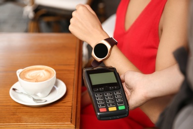 Photo of Woman making payment with smart watch in cafe, closeup