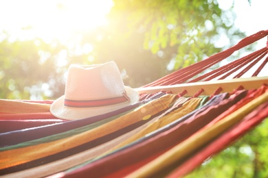 Photo of Bright comfortable hammock with hat hanging in green garden, closeup
