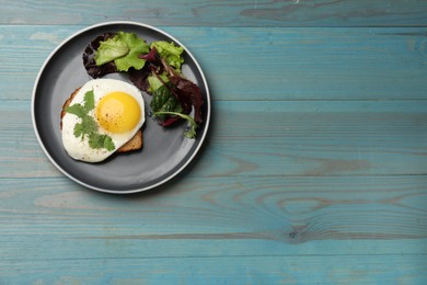 Photo of Plate with tasty fried egg, slice of bread and salad on light blue wooden table, top view. Space for text