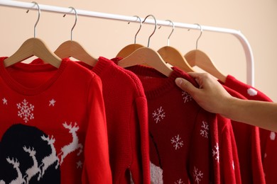 Woman choosing Christmas sweater from rack near beige wall, closeup