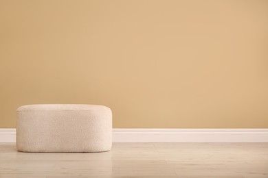 Stylish comfortable pouf near beige wall indoors, space for text