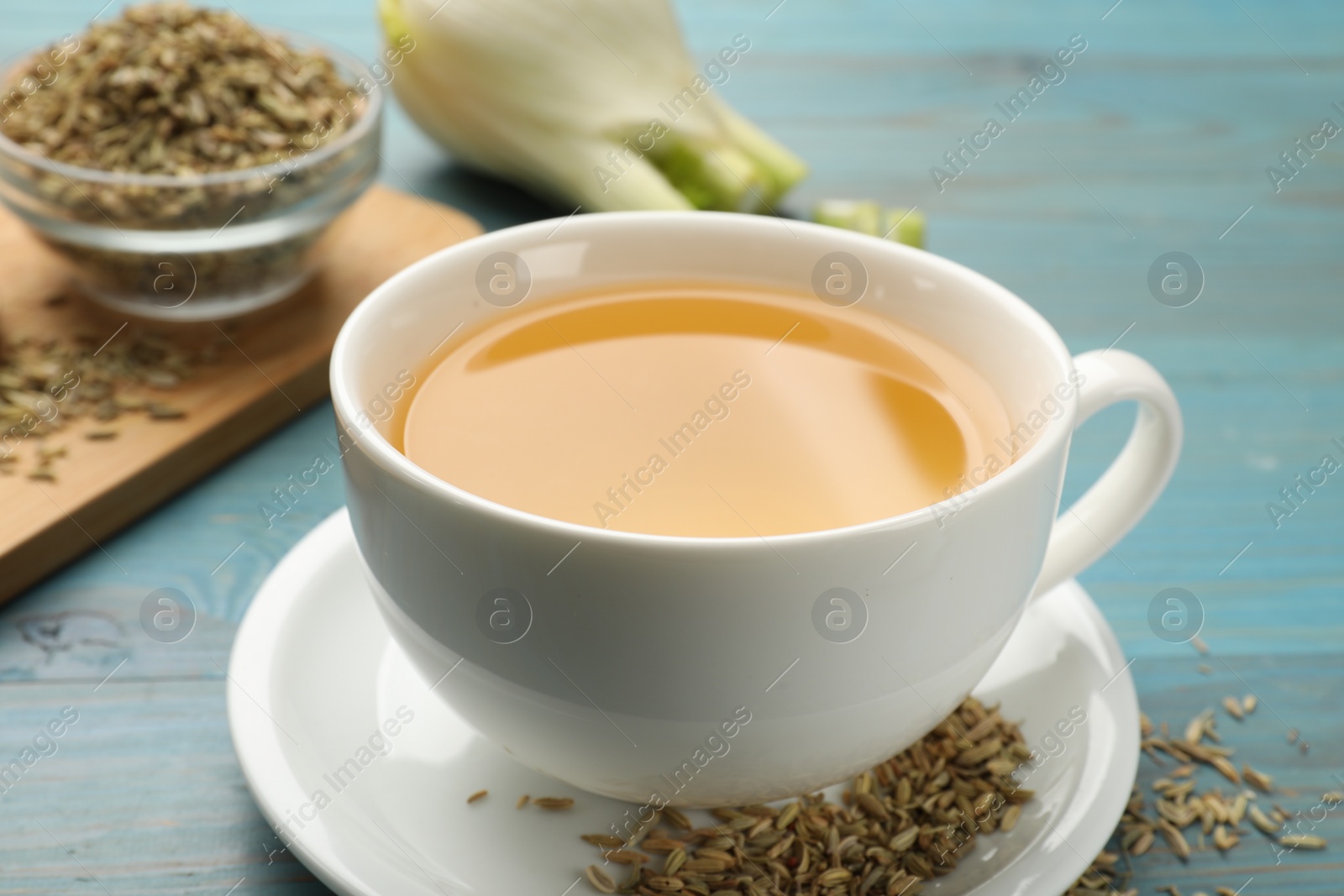 Photo of Fennel tea in cup and seeds on light blue wooden table, closeup