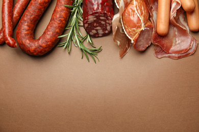 Photo of Different types of sausages with rosemary on brown background, flat lay. Space for text