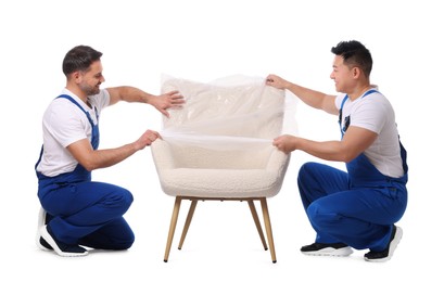 Workers covering armchair with plastic film on white background