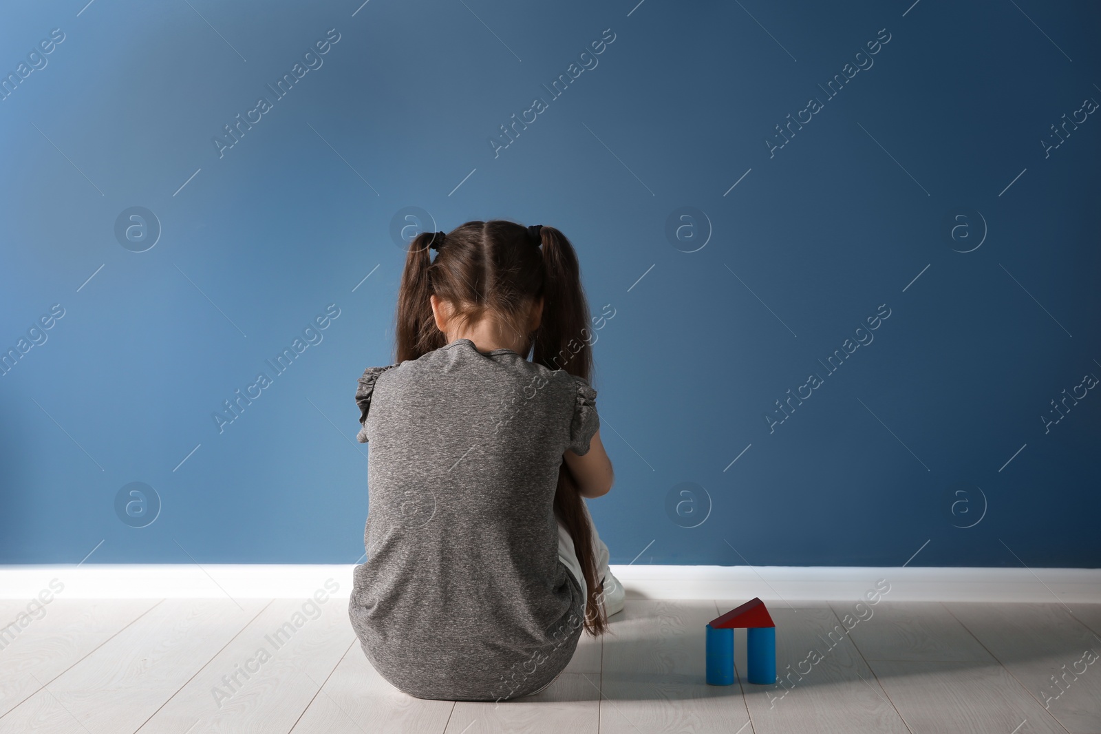 Photo of Little girl with toy sitting on floor near color wall in empty room. Autism concept