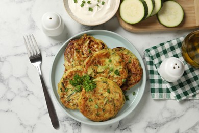 Photo of Delicious zucchini fritters served on white marble table, flat lay