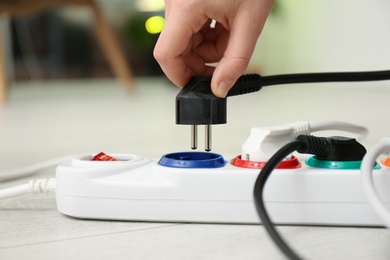 Photo of Woman inserting power plug into extension cord on floor indoors, closeup. Electrician's professional equipment