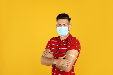 Vaccinated man with protective mask and medical plaster on his arm against yellow background