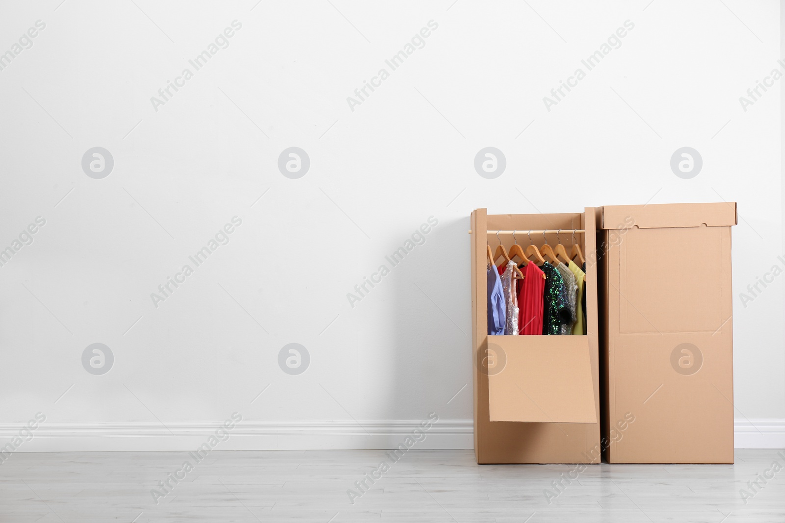 Photo of Wardrobe boxes with clothes against light wall indoors. Space for text