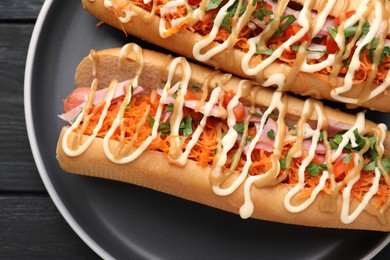 Delicious hot dogs with bacon, carrot and parsley on black table, top view